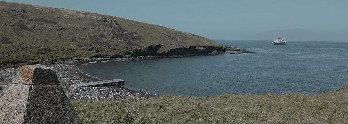 Borne de l'Aviso Bougainville installée en 1939 pour réaffirmer la possession française des Îles Crozet avec une vue sur la manchotière de la Baie du Navire, dans les Terres Australes et Antarctiques Française. Extrait du documentaire "Murmures dans les rugissants" de Lauren Ransan. CC BY-SA 4.0
